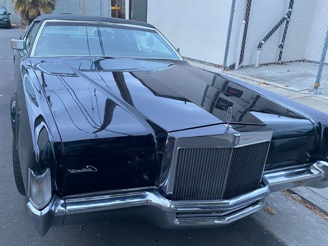 Black vintage luxury car parked outside a building, front view with chrome grille and hood ornament.