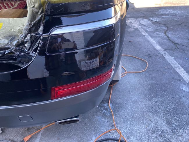 Rear corner of a black car with a damaged headlight, parked on icy pavement with an orange extension cord nearby