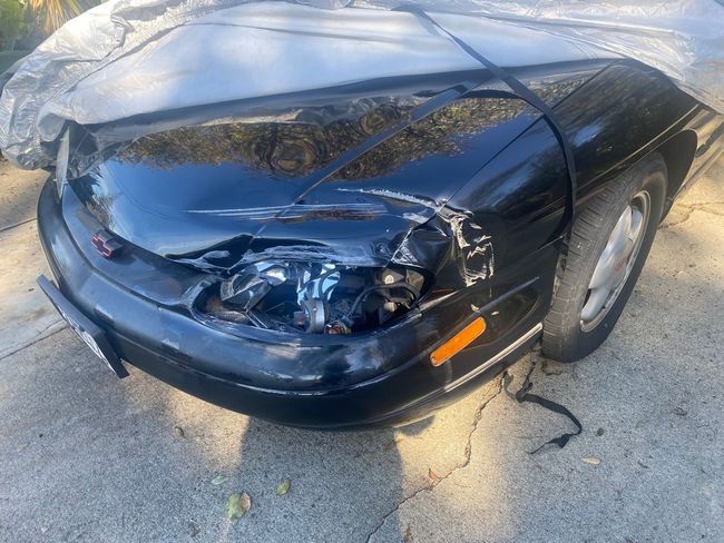 Black car with severe front-right headlight and bumper damage parked on a driveway