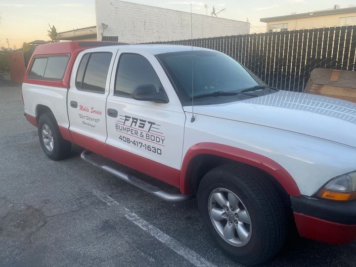 White and red work pickup truck parked outdoors beside a fence at sunset