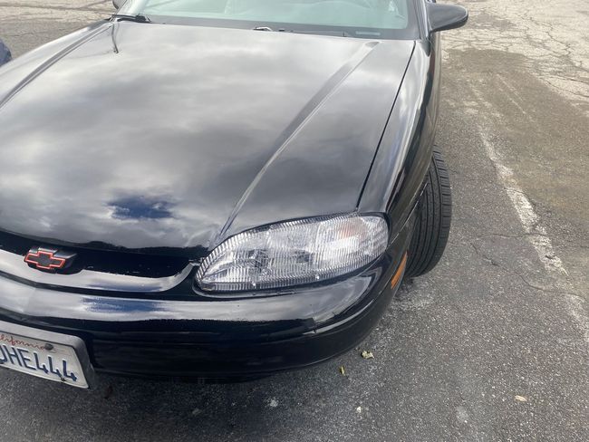 Front view of a black Chevrolet sedan parked on pavement, with a damaged front bumper.