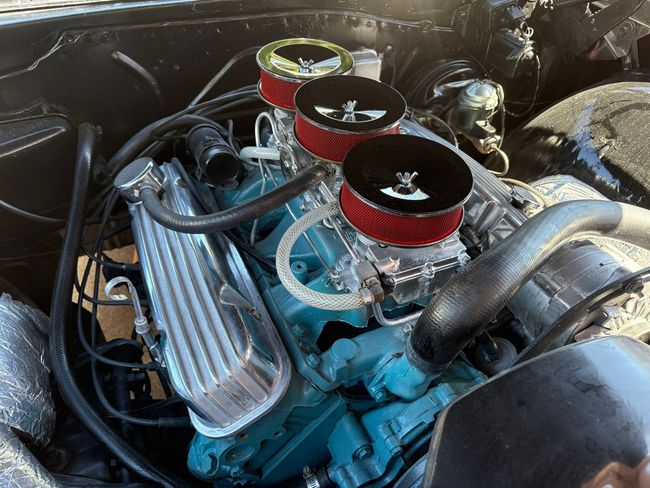 Close-up of a blue engine with red air filters in a car bay, showing chrome pipes and wiring.