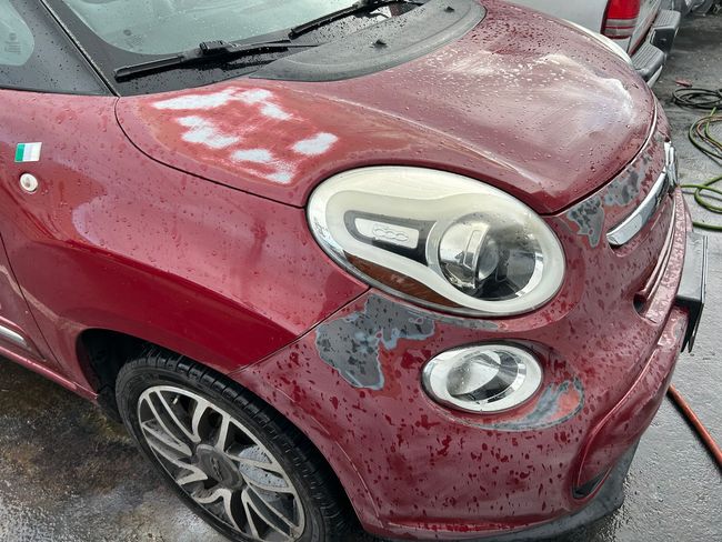Red compact car with hail damage on the hood and front fender in a snowy setting