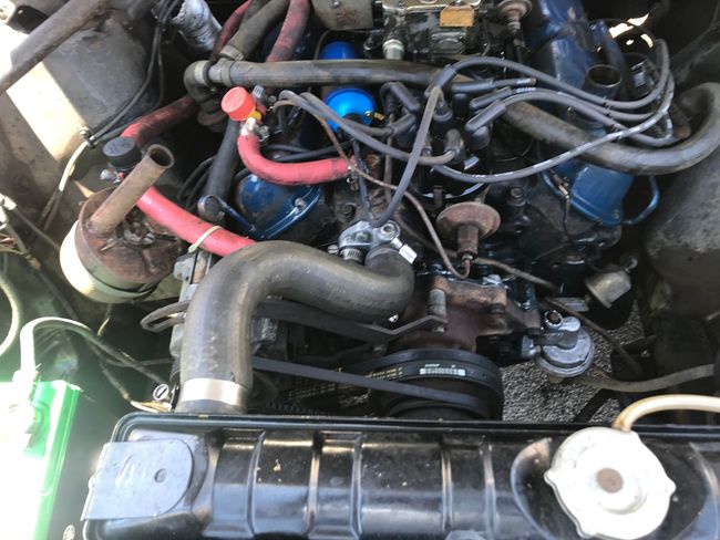 Close-up of a car engine bay with hoses, wiring, and a black air intake assembly.