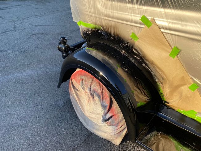 Close-up of a black trailer wheel with red hub under tan cargo wrap, secured with green tape straps