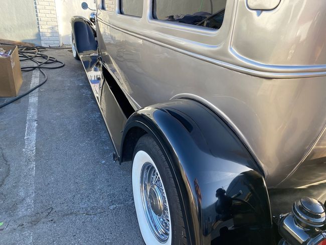 Classic silver car with black fender and whitewall tire, parked outdoors near a building.