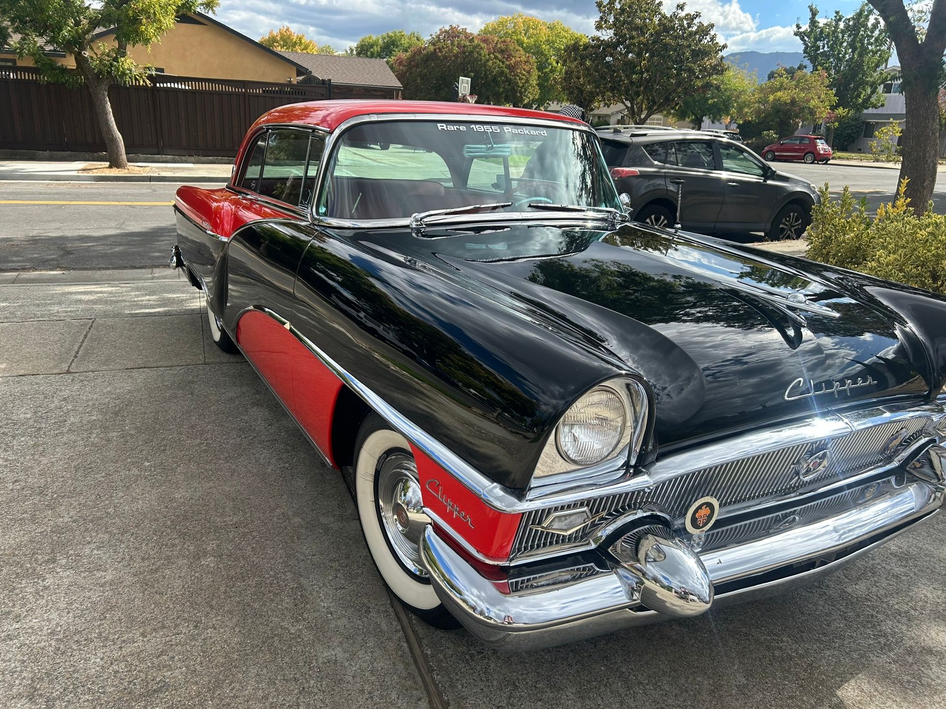 Black classic car with red roof and red side panels parked outdoors in a lot