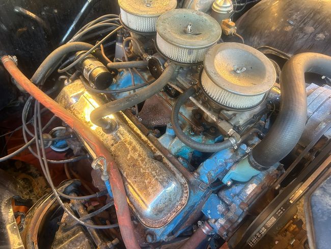 Close-up of a car engine with chrome air filters, blue valve covers, and tangled hoses under warm light