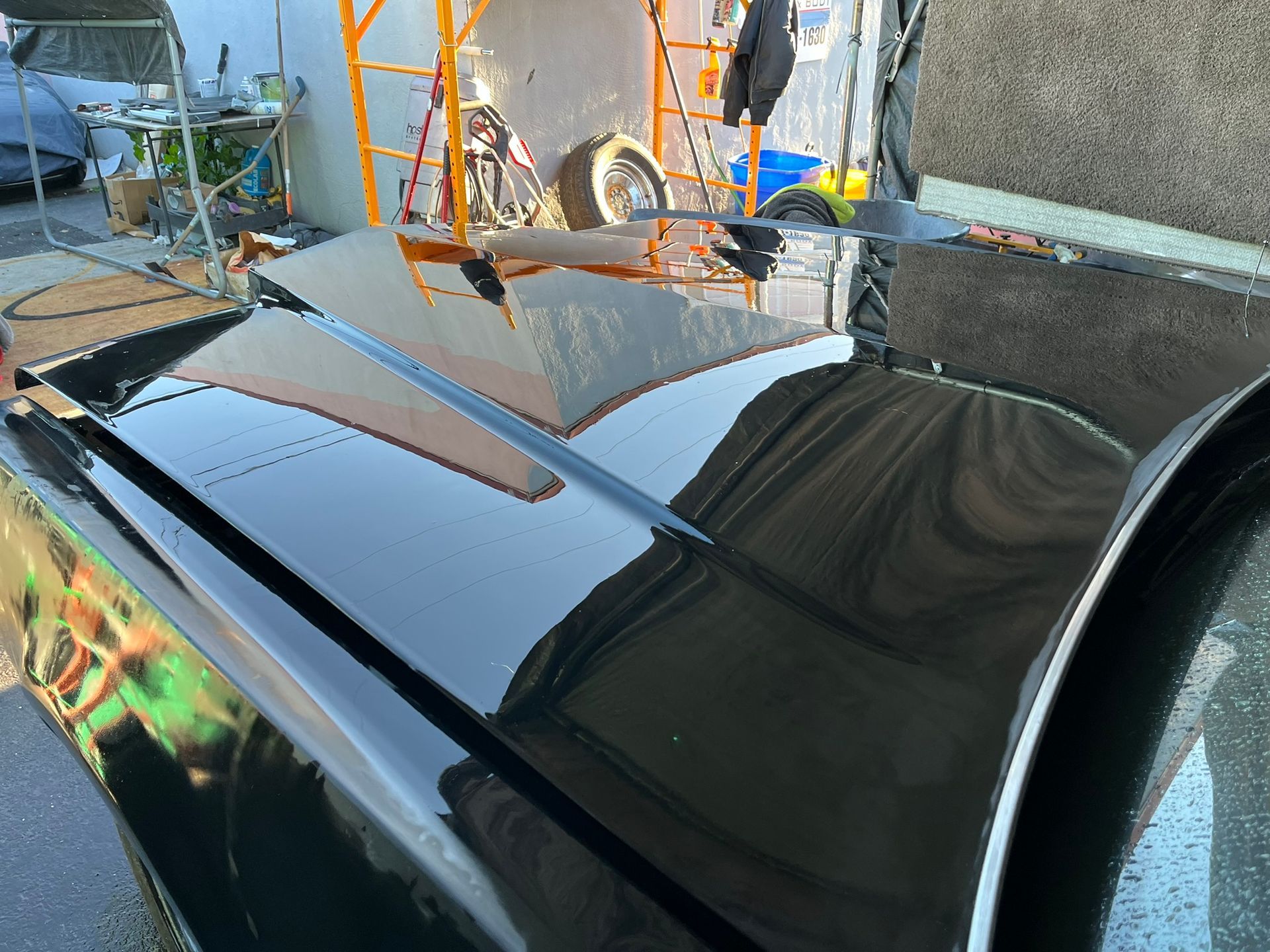 Black car hood with mirror-like reflections in an outdoor workshop setting