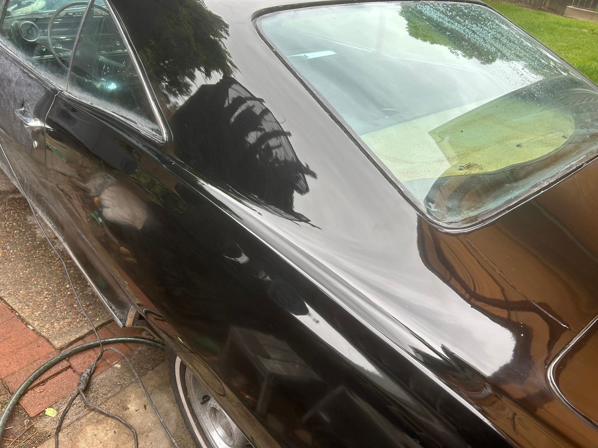 Black car parked on a wet driveway, with a hose on the ground