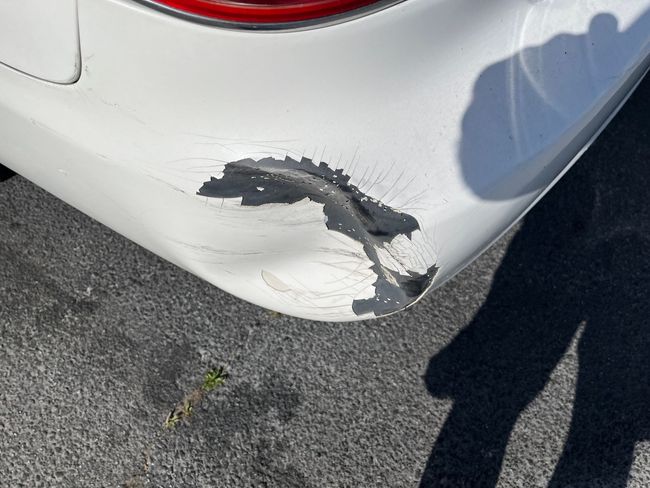 Scratched white car bumper with a large paint chip and scuff marks near the rear light