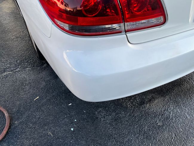 Rear corner of a white car with a red taillight on pavement.