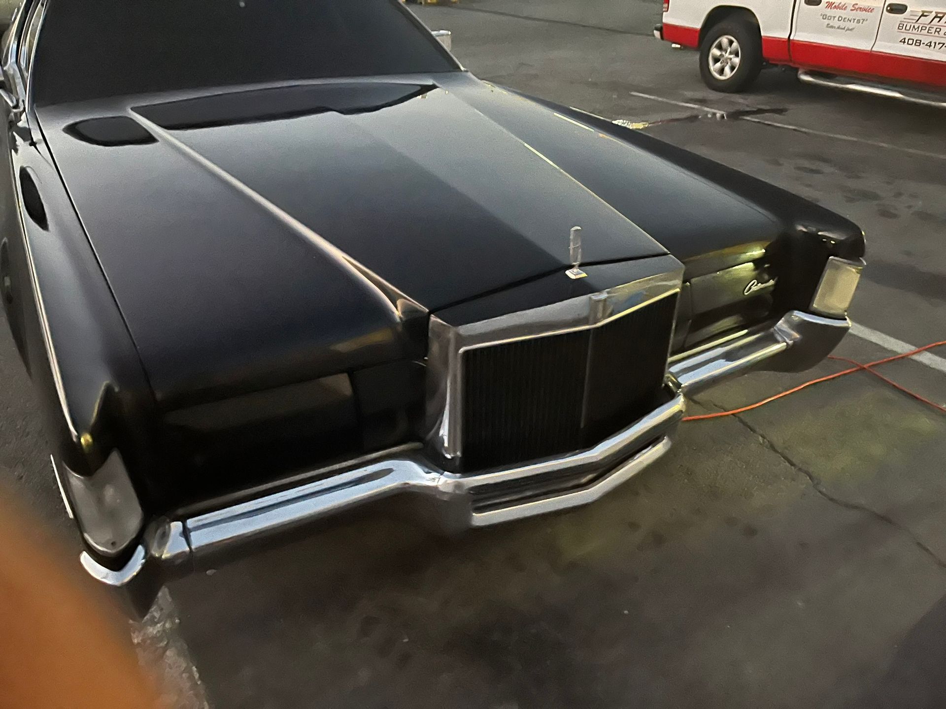 Black vintage luxury car parked on pavement, front view with chrome grille and hood ornament.