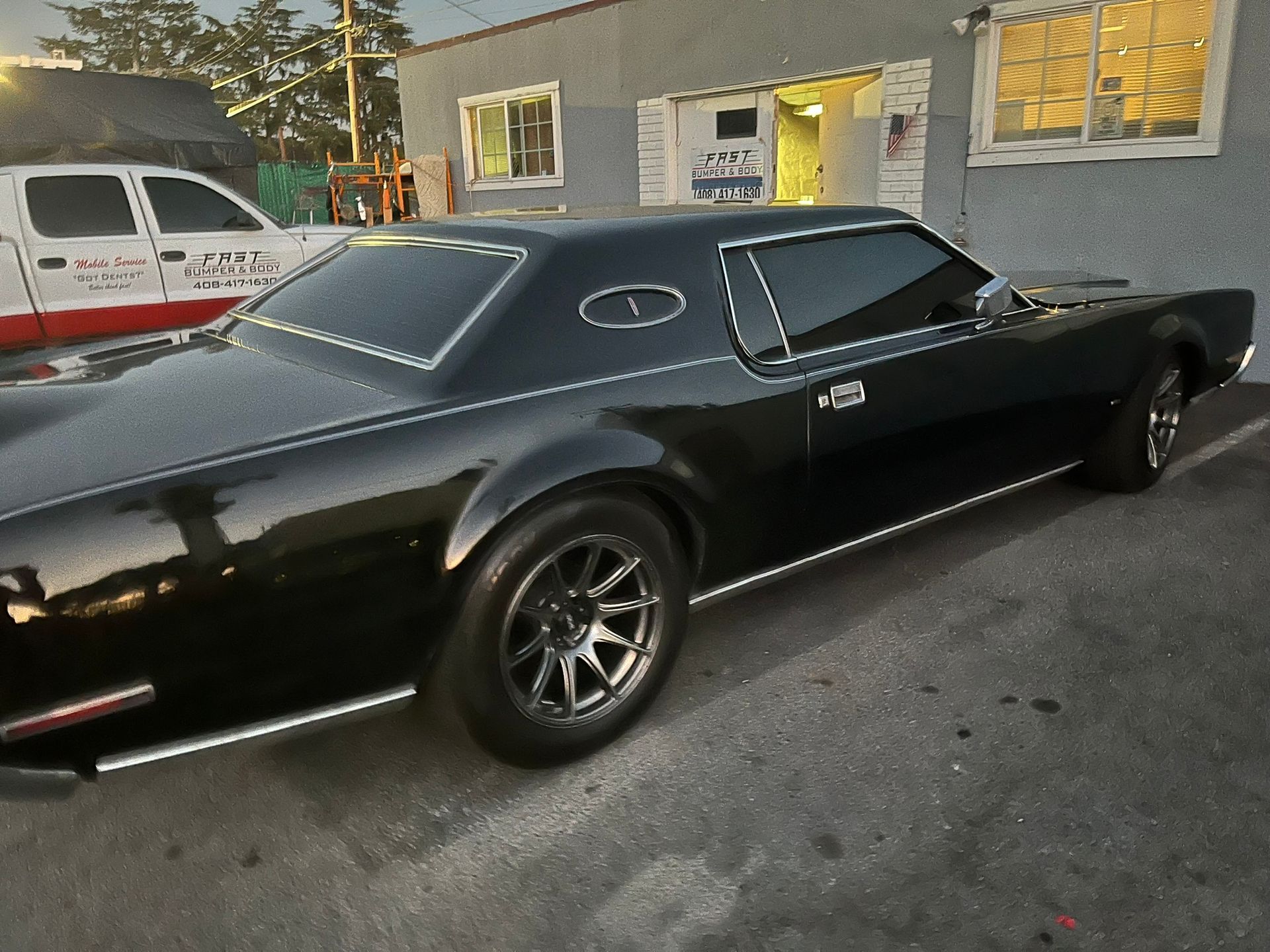 Black classic muscle car parked outside a building at dusk