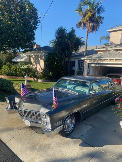 Classic gray vintage car with American flags parked in a sunny suburban driveway.