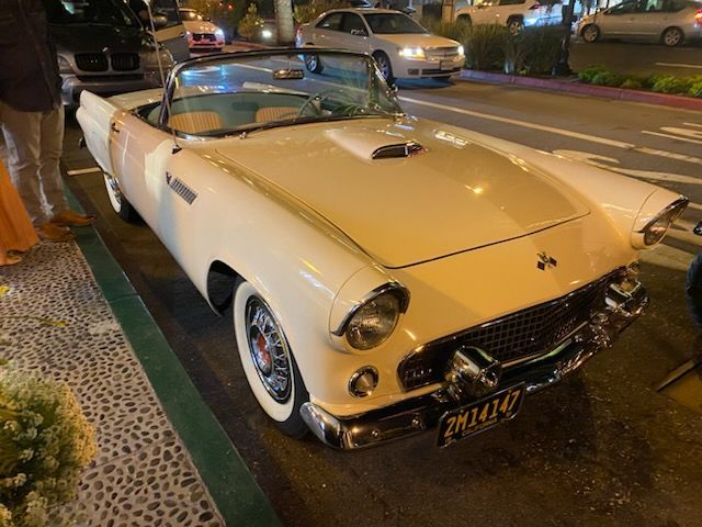 Classic cream convertible parked at night on a city street, with chrome details and whitewall tires.