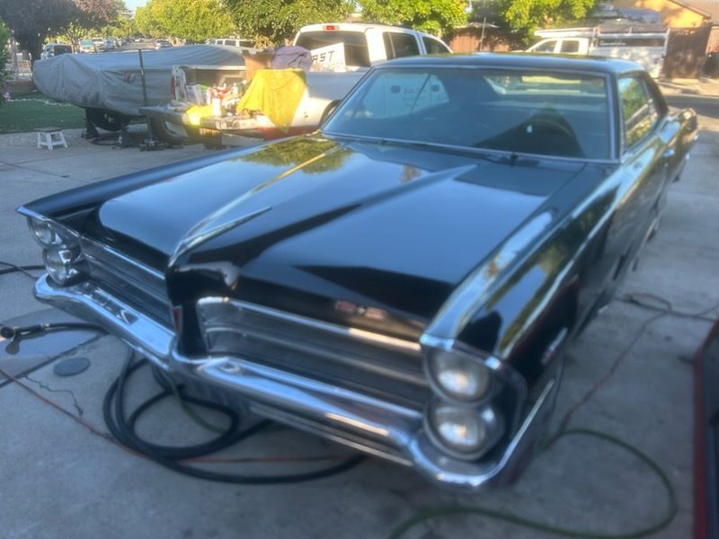 Classic black vintage car with chrome details parked in a driveway, with a trailer and hose nearby