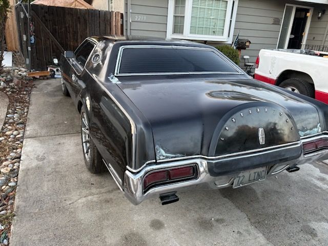 Black classic car parked in a driveway beside a house, rear view
