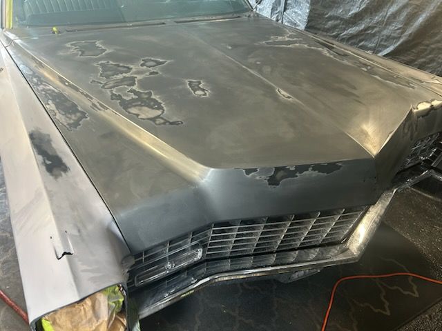 Damaged gray car front end with dented hood and broken grille in a garage