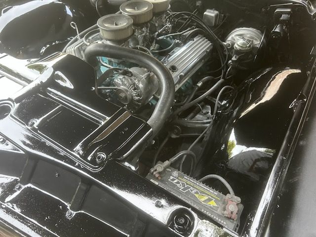 Classic car engine bay with polished black components and chrome air cleaners.