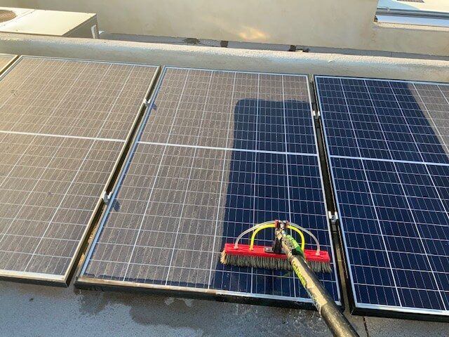 A person is cleaning a solar panel with a brush.
