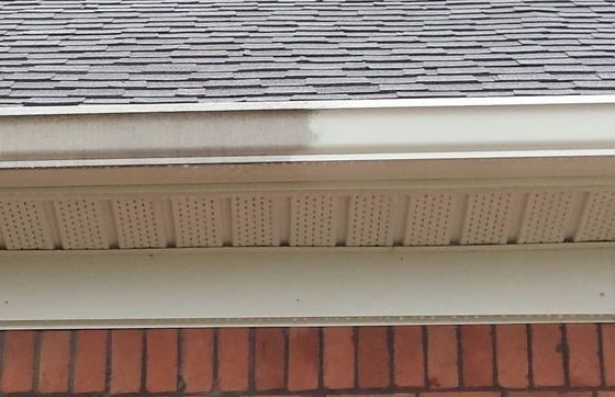A gutter on the side of a brick building with a roof in the background.