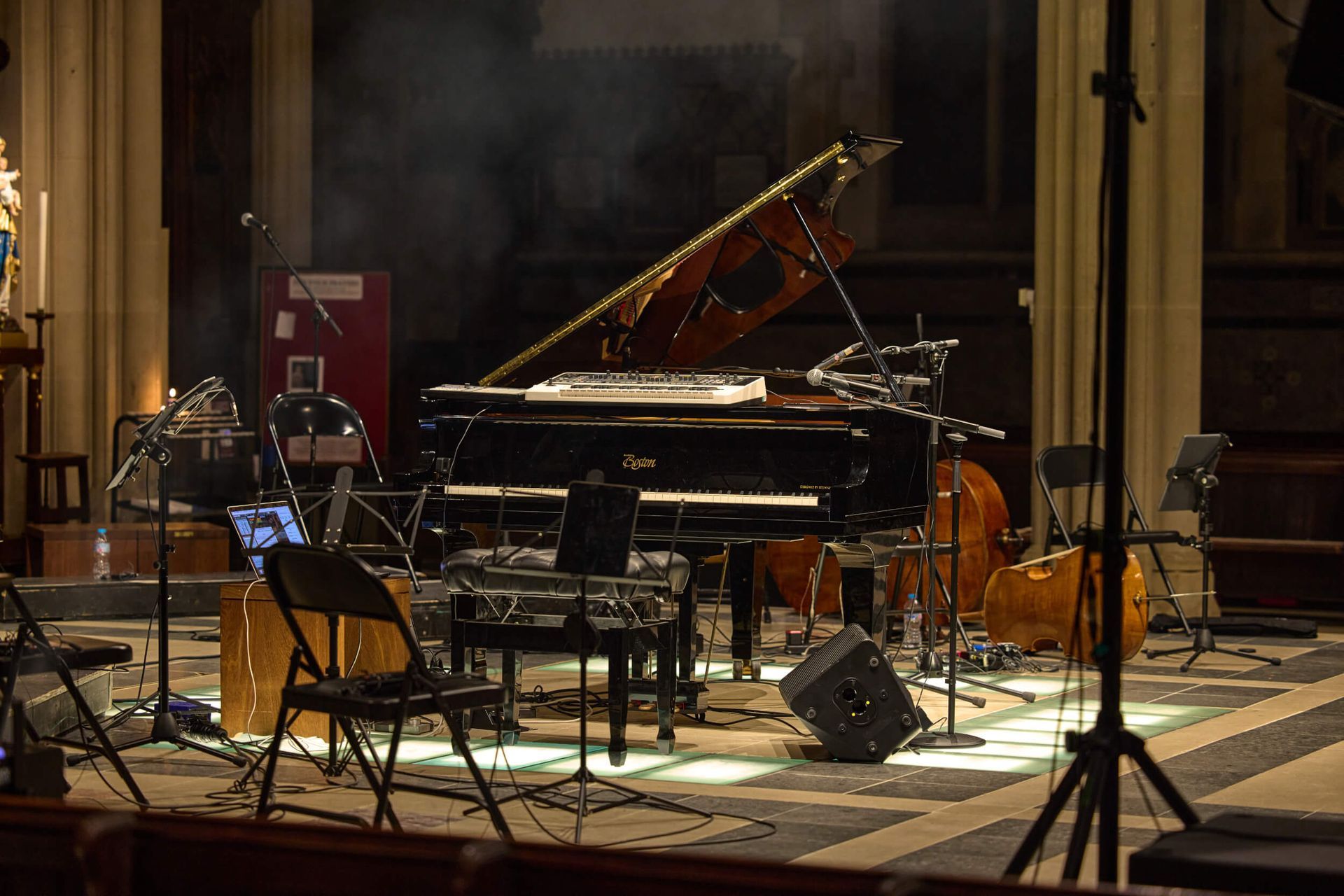 Stage setup with piano, double bass, and equipment in a dimly lit hall, likely for a performance.