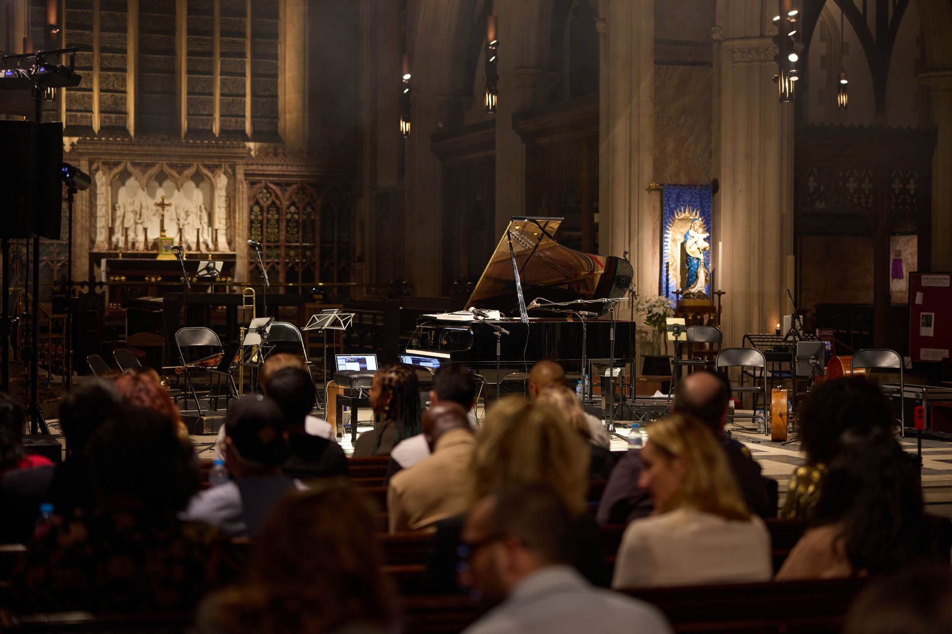 Audience watches a concert with piano on stage in a church. Low lighting.