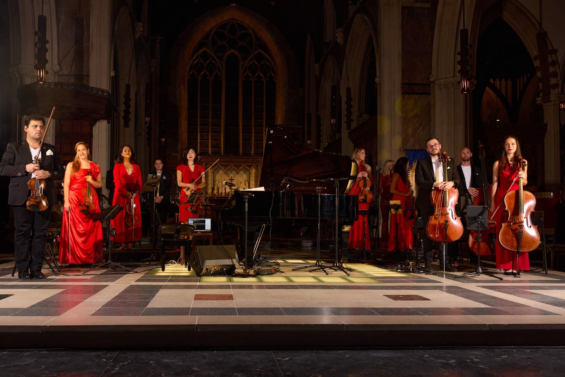 A string orchestra performs on stage in a church. Musicians wear formal attire, lit by stage lights.
