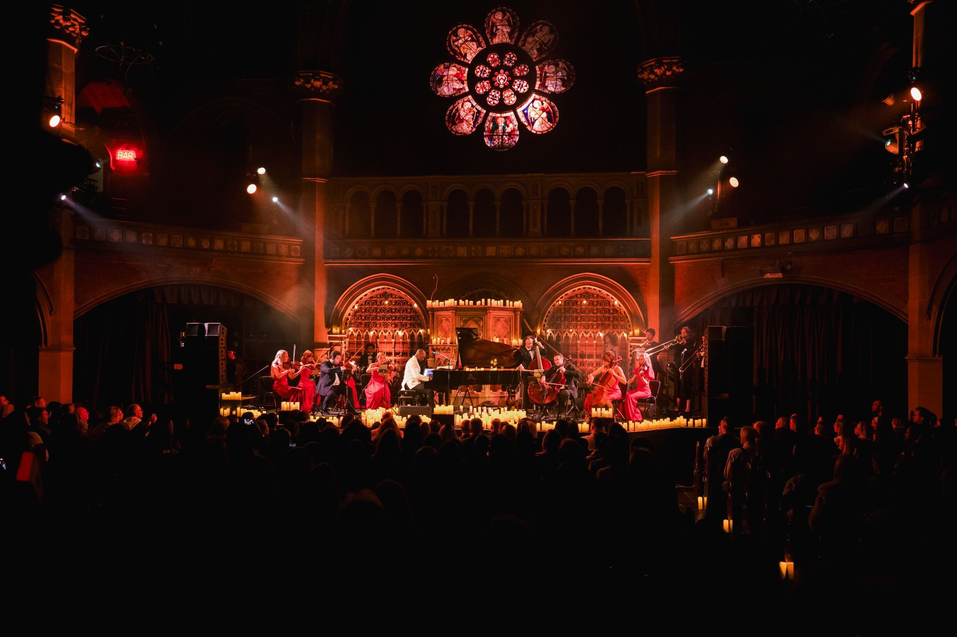 Musical performance on stage in a gothic style building, with a stained glass window.