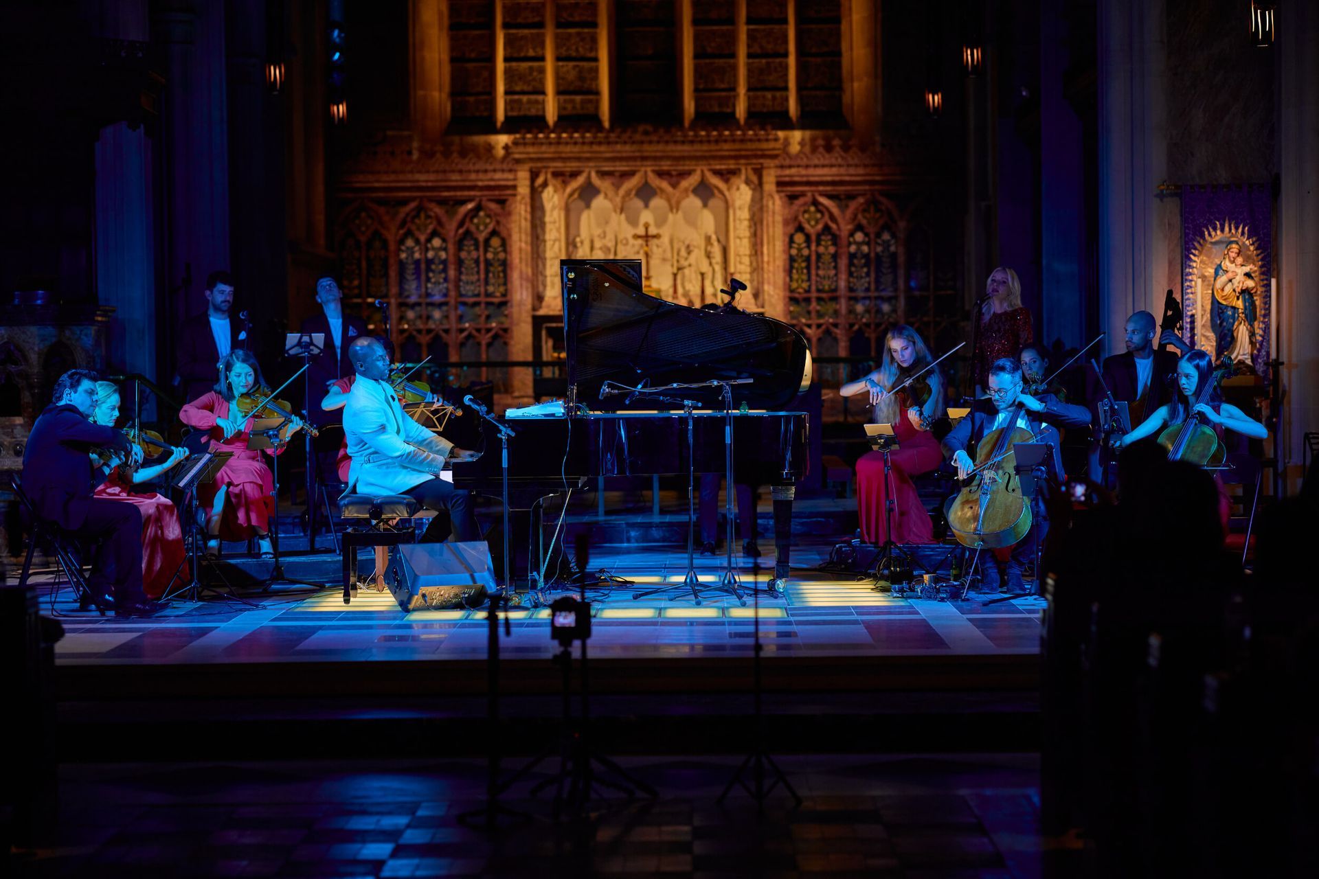 An orchestra performs on a stage in a church, lit with blue and gold hues.