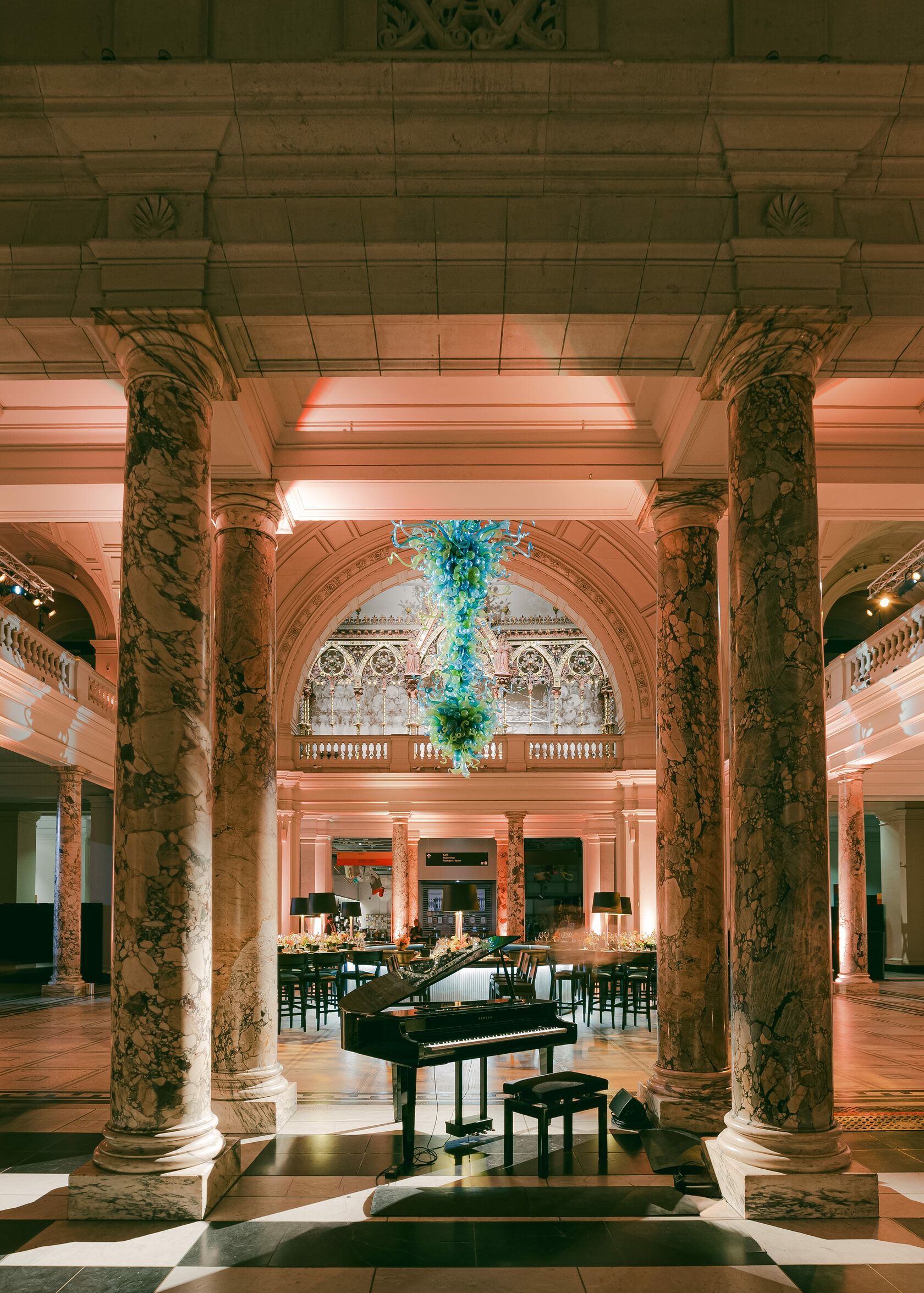 Grand hall with marble columns, piano, and colorful glass art.