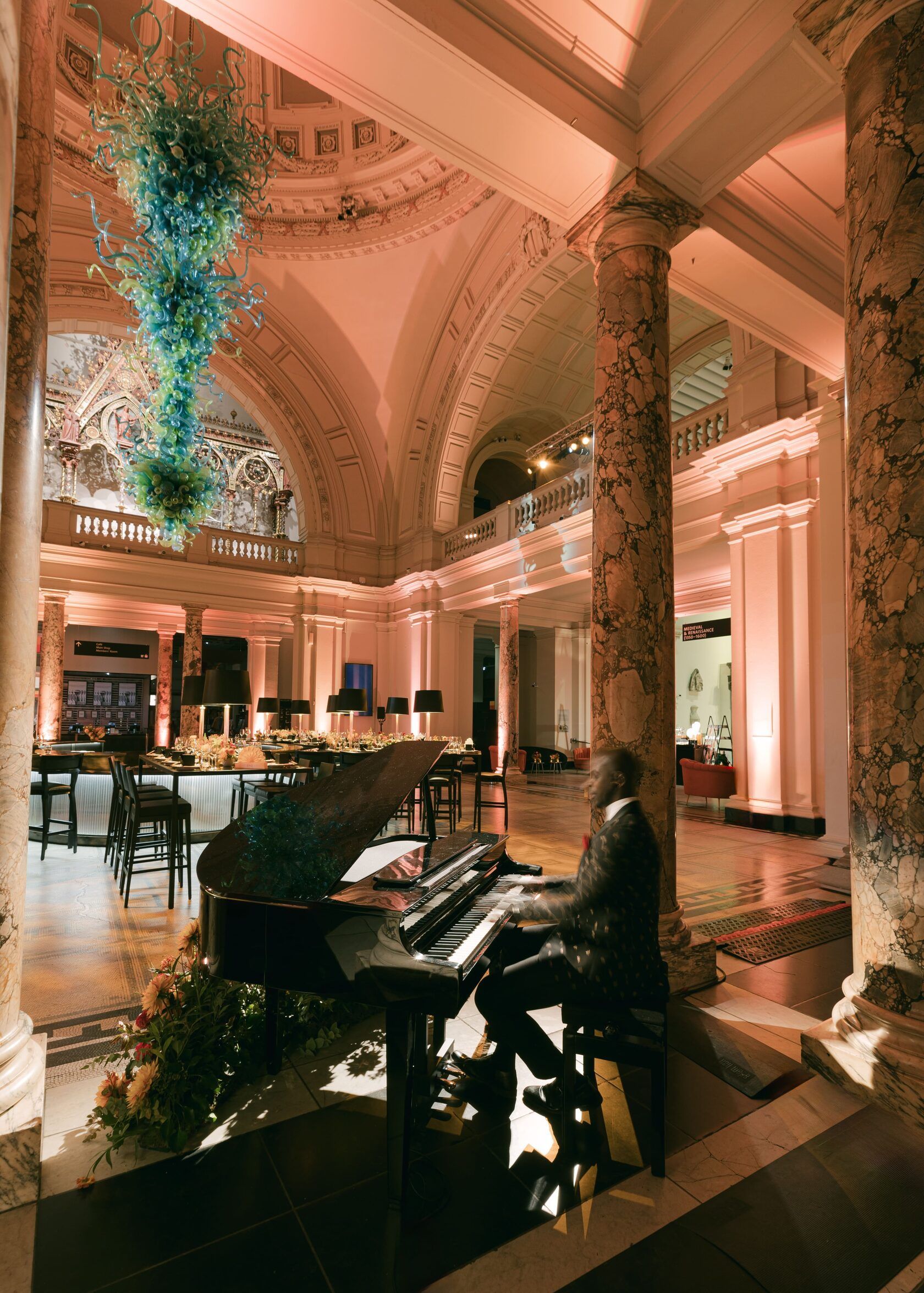 Pianist playing grand piano in a formal hall with columns and dome ceiling, illuminated by warm lighting.