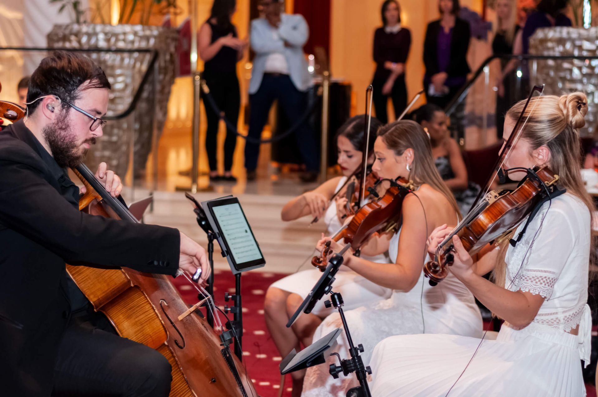 A string quartet performing, with a cellist and three violinists, in a formal setting.
