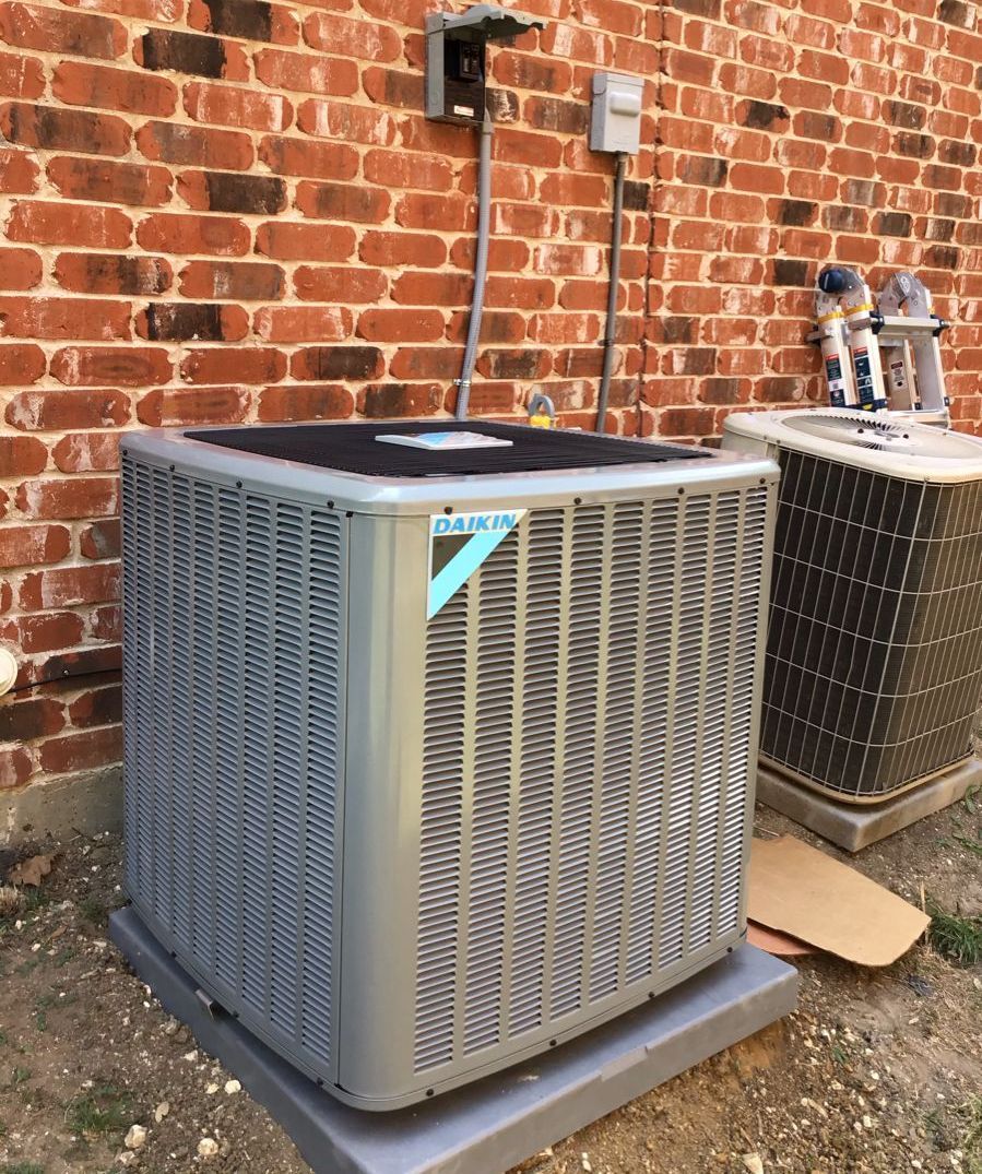 Daikin air conditioning unit on a concrete pad next to a brick wall and an older unit.