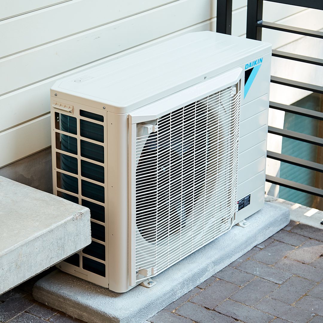 White and blue Daikin air conditioner unit on a concrete pad next to a building.