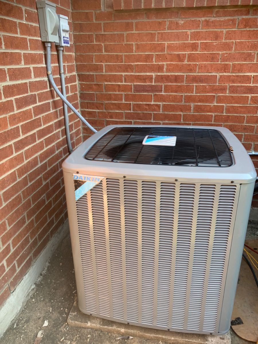 Air conditioner unit outside a brick building with electrical box.