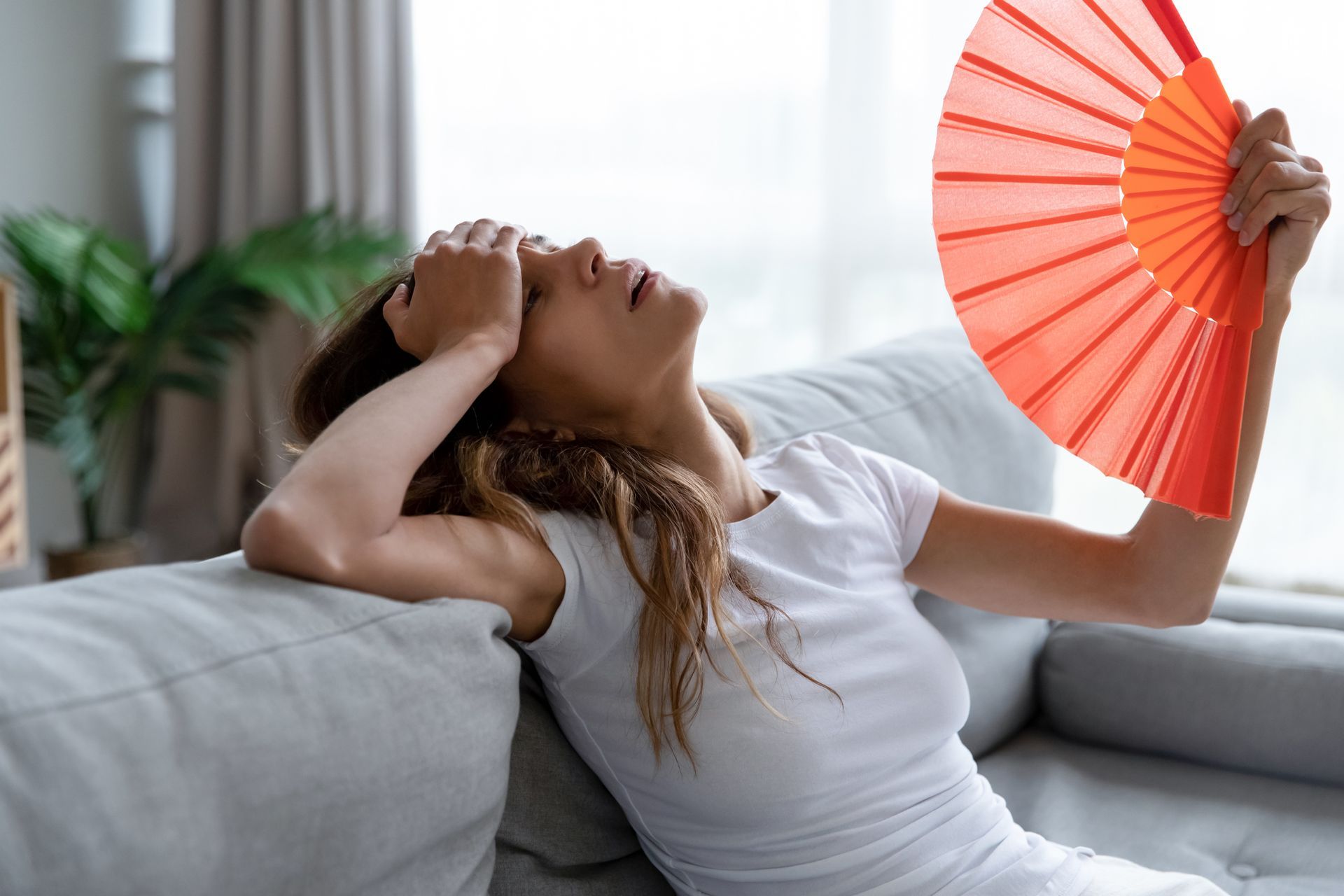 Woman feeling overheated indoors while using a handheld fan during a Texas summer heat wave.