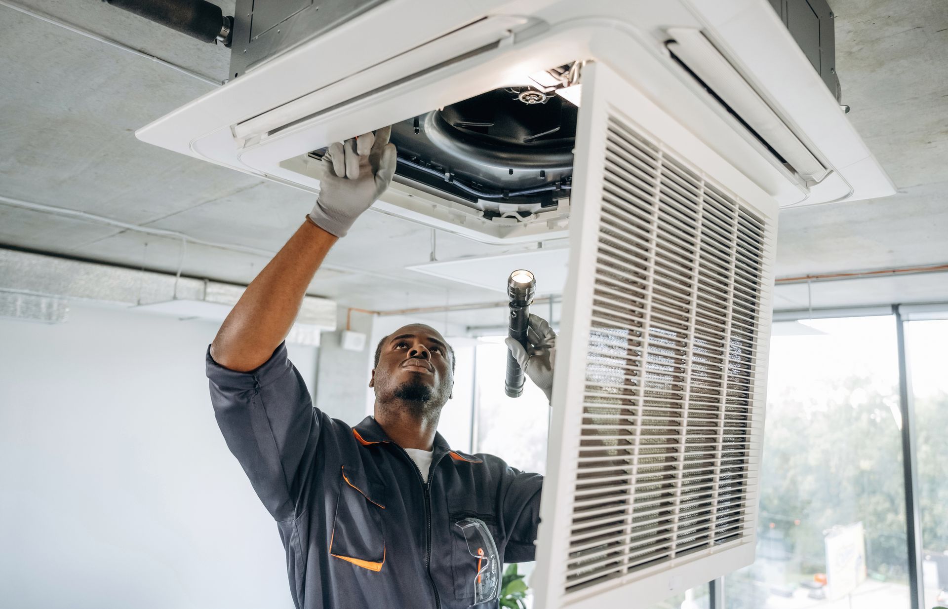 Airmax technician inspecting a commercial overhead air vent unit with a flashlight.