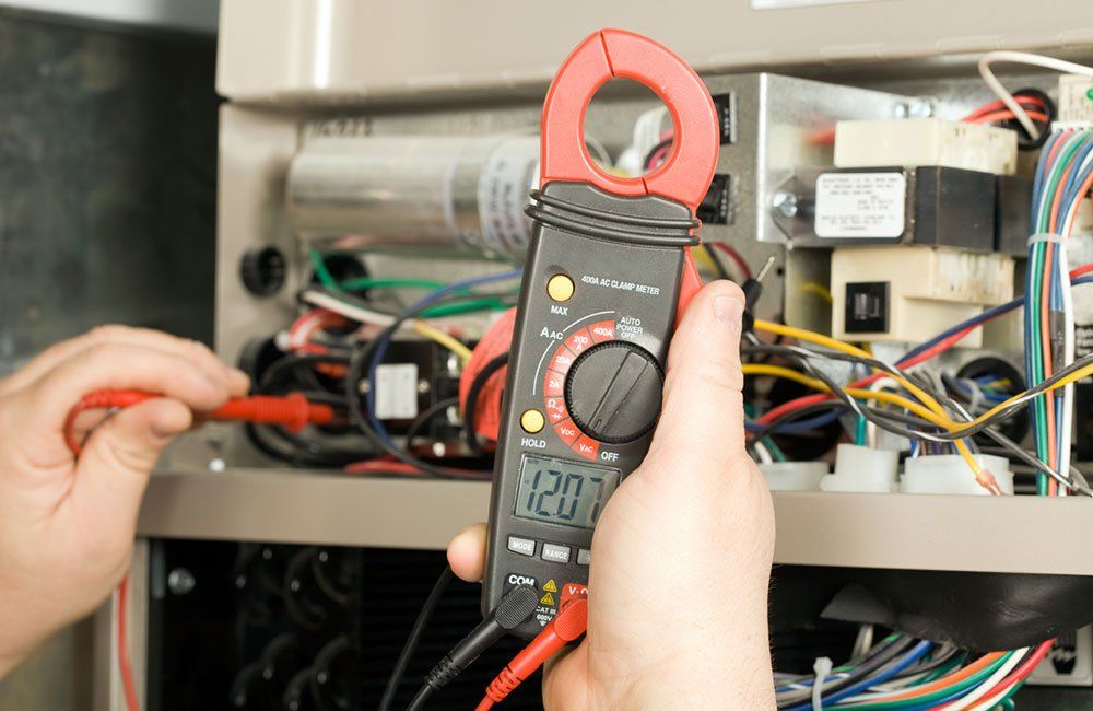 A person uses a multimeter to test electrical components inside a furnace.
