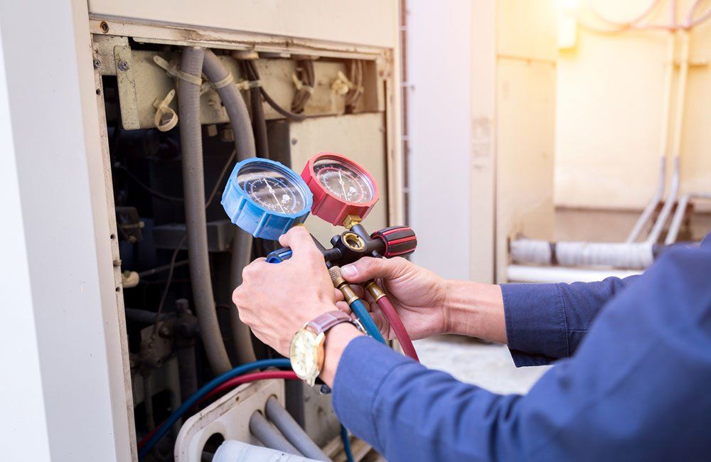 A person in a blue shirt uses gauges to check an air conditioning unit.