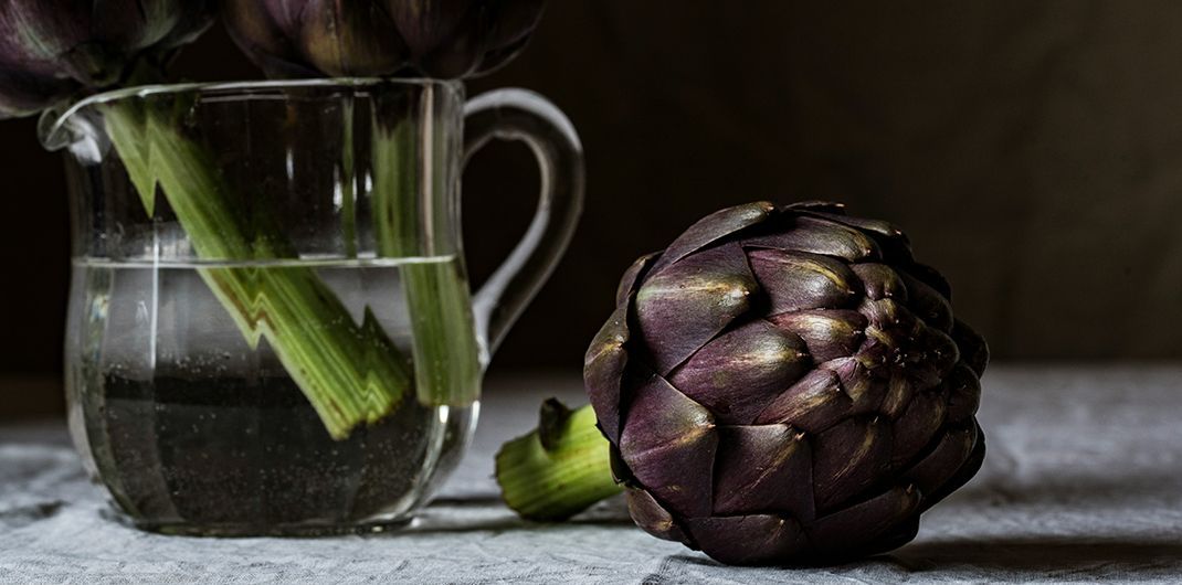 An artichoke is sitting next to a pitcher of water on a table.