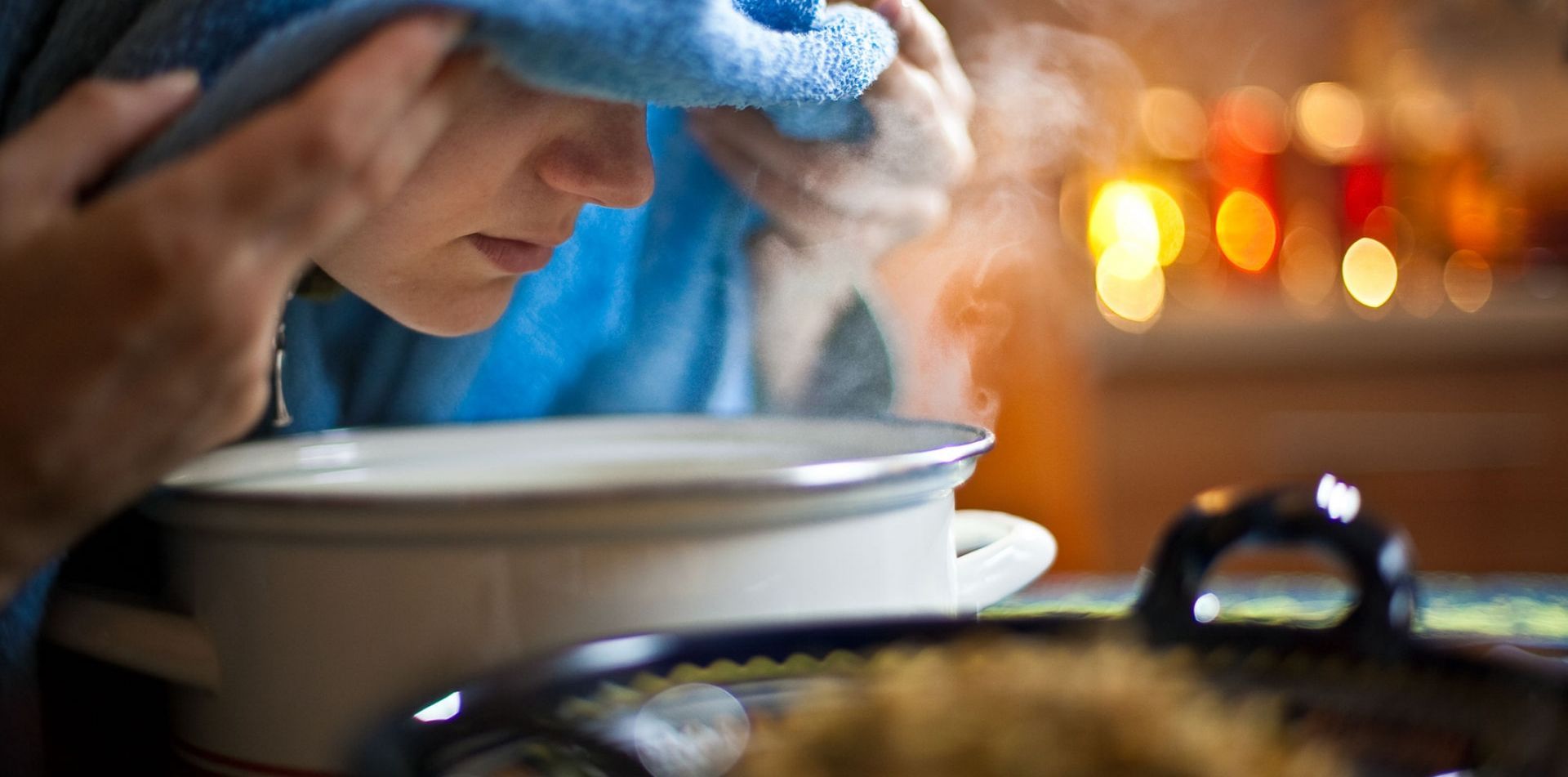A woman is steaming her face with a towel over her head.
