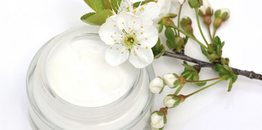 A jar of cream next to a flower on a white surface.