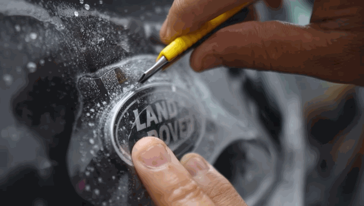 Close-up of a technician using a blade to trim paint protection film around the Land Rover badge on a vehicle.
