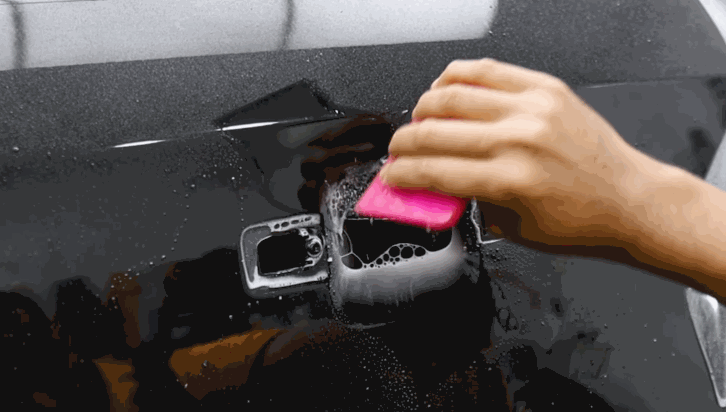 A person uses a pink squeegee to smooth and press paint protection film around a car’s recessed door handle.