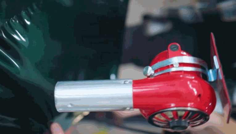 A red and silver heat gun is used to apply a glossy green vinyl wrap to a vehicle surface, helping the material conform smoothly to curves.