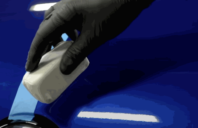 A person applying clay bar to a blue car's surface to prepare for ceramic coating.
