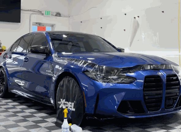 A blue BMW with partially applied paint protection film (PPF) on its front bumper and fender, showcasing the installation process.