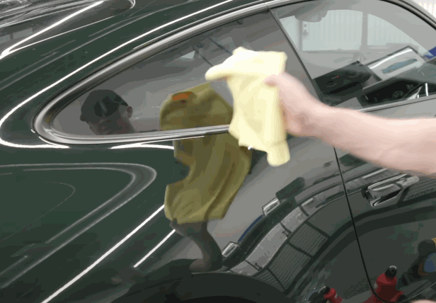 A person wiping down a black car with a microfiber cloth to remove excess moisture before applying paint protection film (PPF).
